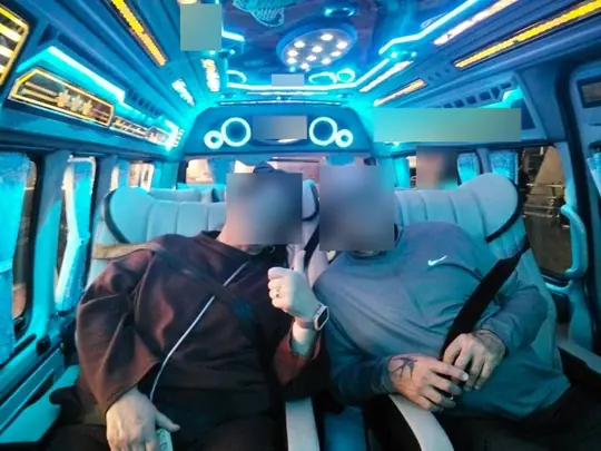 2026년 10월 6일, 파란 LED 조명과 거울 천장 패널 아래 VIP 캐빈에 나란히 앉은 두 손님, 한 명은 얼굴 옆으로 손을 들어 보이고 있다
